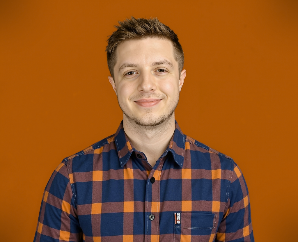 A person smiling in a plaid shirt with orange and blue colors against an orange background.