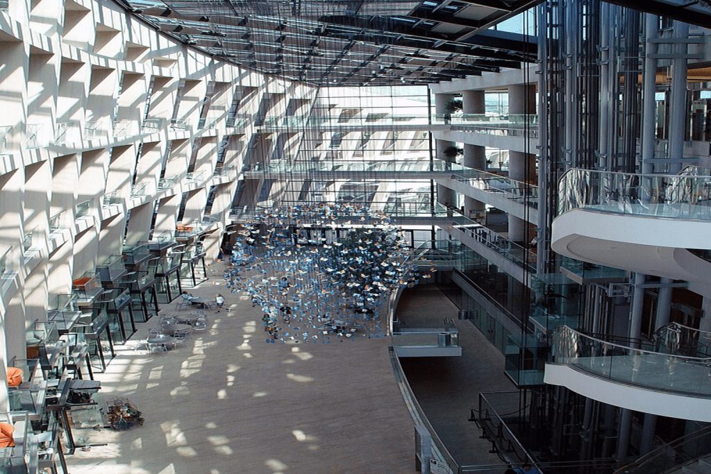 Interior view of a modern library showcasing spacious design with large windows, rows of bookshelves, and an artistic installation hanging from the ceiling.